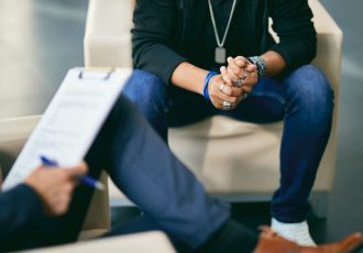 Close-up image of a veteran sitting in therapy, hands clasped, symbolizing the beginning of healing through professional mental health care.