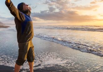 A man with arms outstretched enjoying the freedom of a sunset on the beach, symbolizing the emotional relief and joy of starting a new chapter after treatment.