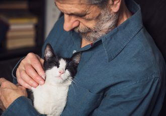 A veteran gently holding a relaxed black-and-white cat, emphasizing the calming presence of pets in a veteran’s mental health journey at Solara Mental Health.