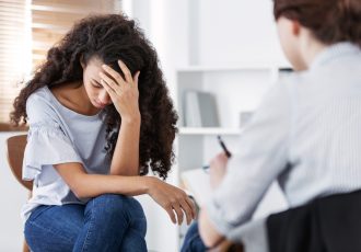 A young woman holding her head during a therapy session, symbolizing emotional distress and professional care.