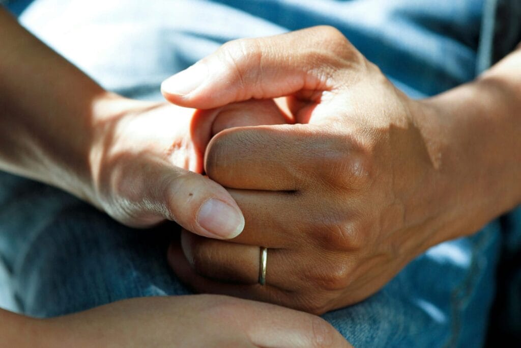 Close-up of hands gently holding each other, representing comfort and emotional support.